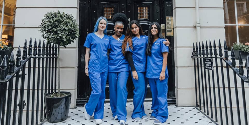 Four nurses in blue scrubs outside a Georgian clinic entrance for EMface facial toning in Amsterdam